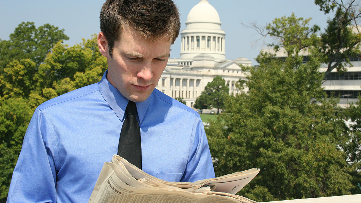 Man reading a newspaper in front of a government building.